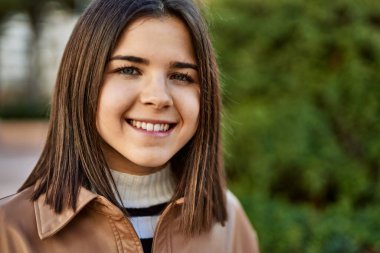 Genç, güzel, esmer kadın dışarıda mutlu bir şekilde gülümsüyor.