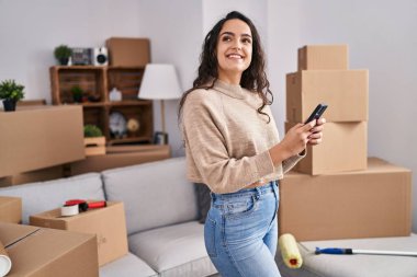 Genç İspanyol kadın yeni evinde akıllı telefon kullanıyor.