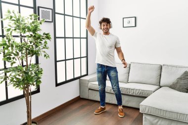 Genç İspanyol adam evde müzik dinlerken kendinden emin gülümsüyor.