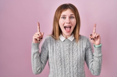 Pembe arka planda duran güzel bir kadın. Gülümsüyor, şaşırıyor, parmaklarıyla işaret ediyor ve kollarını kaldırıyor.. 