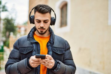 Yakışıklı, sakallı, mutlu ve kendine güvenen, akıllı telefon kullanan, kışlık palto giyen bir İspanyol.