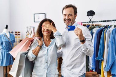 Hispanic middle age couple holding shopping bags and credit card smiling and laughing with hand on face covering eyes for surprise. blind concept. 