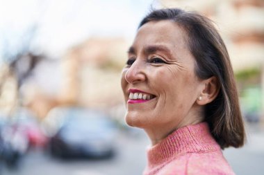 Orta yaşlı bir kadın sokakta kendine güvenerek gülümsüyor.