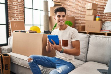 Yeni evindeki koltukta oturan dokunmatik ped kullanan İspanyol genç adam.