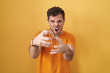 Sarı arka planda dikilen İspanyol genç adam öfkeyle bağırıyor, elleri boğazlamaya çalışıyor, deli gibi bağırıyor. 