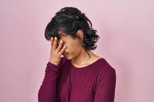 Young beautiful woman standing over pink background with sad expression covering face with hands while crying. depression concept.