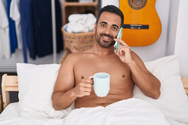 Junger Hispanischer Mann Spricht Auf Smartphone Kaffee Trinkend Schlafzimmer Liegend — Stockfoto