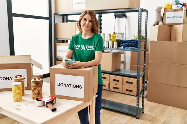 Mulher Voluntária Meia Idade Usando Smartphone Doações Stand Olhando Positivo — Fotografia de Stock