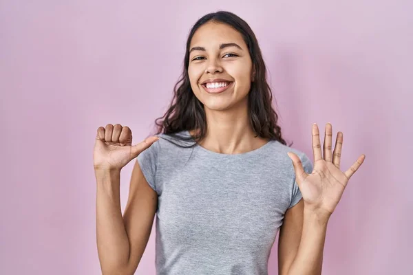 Young brazilian woman wearing casual t shirt over pink background showing and pointing up with fingers number six while smiling confident and happy.