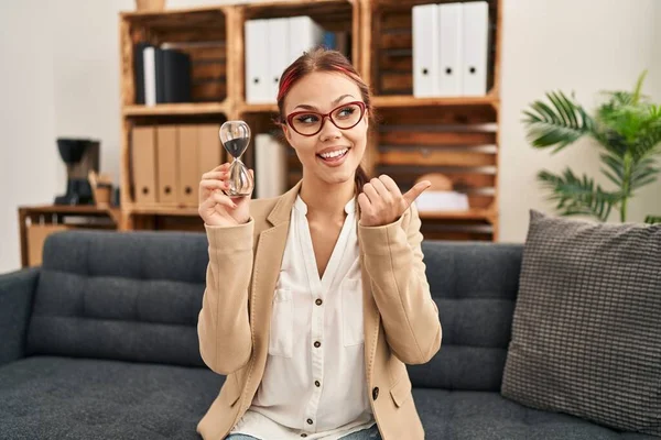 Young Caucasian Woman Working Counselor Holding Sand Clock Pointing Thumb — 스톡 사진