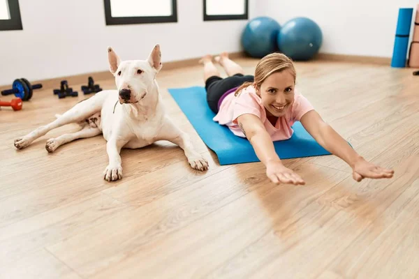 Young caucasian woman smiling confident stretching with dog at sport center