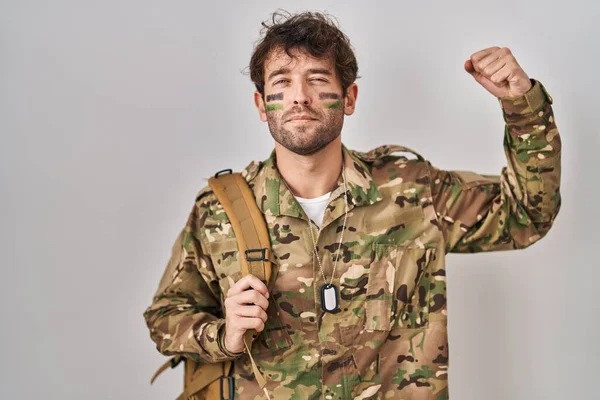 Hispanic young man wearing camouflage army uniform strong person showing arm muscle, confident and proud of power