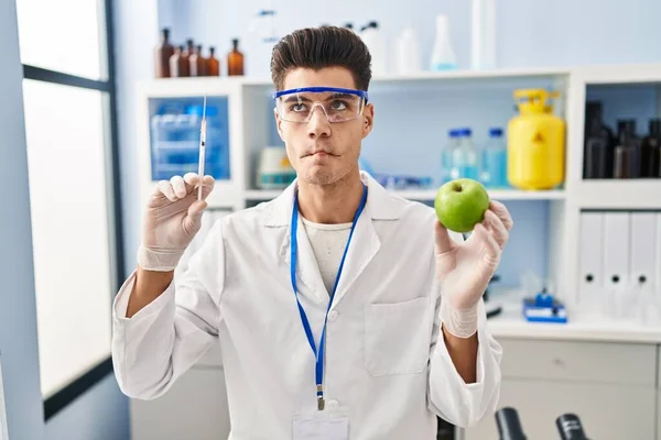 Young Hispanic Man Working Scientist Laboratory Holding Apple Making Fish — ストック写真