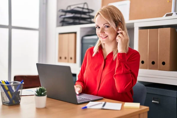 Young blonde woman business worker using laptop and earphones at office
