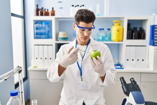 Young Hispanic Man Wearing Scientist Uniform Injecting Apple Laboratory — Stock fotografie
