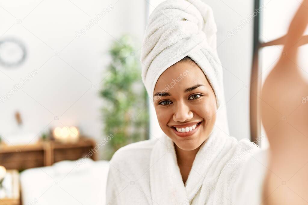 Young latin woman wearing bathrobe make selfie by the camera at beauty center