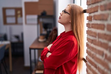 Genç, kızıl saçlı, iş kadını, kollarını kavuşturup ofiste el kol hareketi yapıyor.