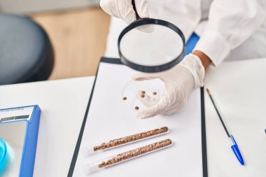 Young hispanic woman scientist looking sample using loupe at laboratory