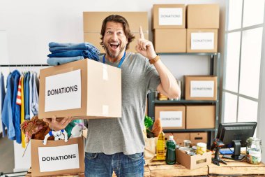 Handsome middle age man holding donations box for charity at volunteer stand pointing finger up with successful idea. exited and happy. number one. 