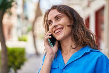 Gülümseyen genç bir kadın caddedeki akıllı telefondan konuşuyor.