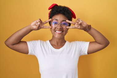 Sarı arka planda dikilen genç Afro-Amerikalı kadın barış sembolü yapıyor. Yüzünde parmakları, gülümseyerek zaferini gösteriyor. 