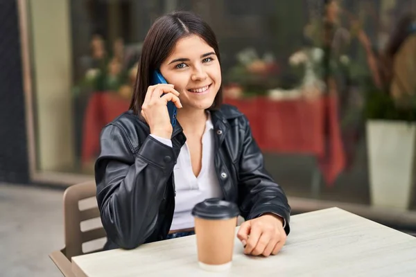 若い美しいヒスパニック系の女性がコーヒーショップテラスでテーブルの上に座っているスマートフォンで話しています — ストック写真