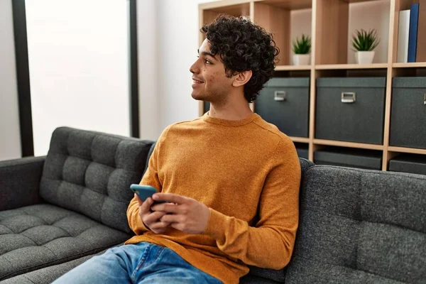 Jonge Spaanse Man Met Smartphone Zittend Bank Thuis — Stockfoto