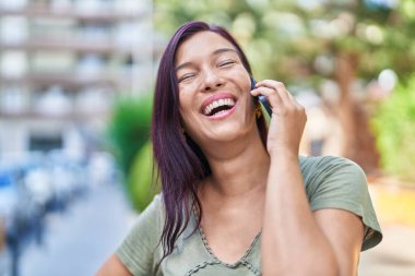 Genç, güzel, İspanyol bir kadın gülümsüyor ve caddede akıllı telefondan konuşuyor.