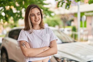 Kendine güvenen genç bir kadın caddede kollarını kavuşturmuş duruyor.