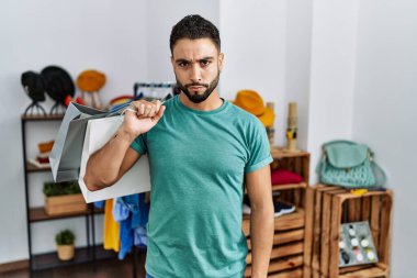 Satış mağazasında sakallı, alışveriş torbası tutan genç yakışıklı, şüpheci ve gergin, sorun yüzünden üzgün. negatif kişi. 