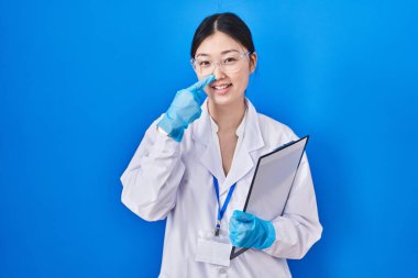 Laboratuvarda çalışan Çinli genç bir kadın, parmaklarını birbirine göstererek neşeli bir şekilde gülümsüyor. güzellik konsepti 