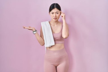 Spor kıyafetleri ve havlu giyen Çinli genç bir kadın avuç içinin açık olmasından rahatsız ve kafası karışmış bir şekilde fotokopi alanını gösteriyor ve alnını işaret ediyor. Bunu bir düşün.. 