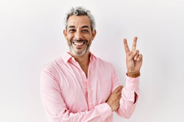 Orta yaşlı İspanyol bir adam izole edilmiş arka planda durup kameraya bakıp gülümsüyor ve zafer işareti yapıyor. İki numara.. 