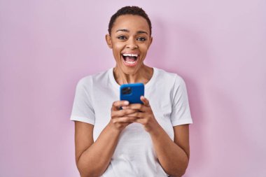 Güzel afro-amerikan kadını akıllı telefon kullanarak çılgın ve hayret verici başarıyı kutluyor gözleri açık heyecanla bağırıyor. 