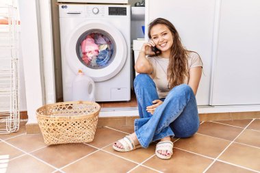 Genç İspanyol kız akıllı telefonda konuşuyor evde çamaşır makinesini bekliyor.