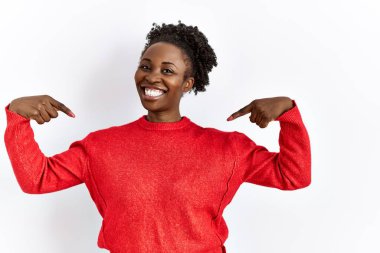 Genç Afro-Amerikalı kadın izole edilmiş arka planda gündelik giysiler giyiyor. Yüzünde bir gülümsemeyle, kendini gururlu ve mutlu olarak gösteriyor.. 