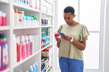 Afro-Amerikalı kadın müşteri eczanede akıllı telefon kullanıyor.