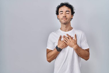 Soyutlanmış arka planda duran İspanyol bir adam elleri göğsünde, gözleri kapalı ve yüzünde minnet dolu bir jest ile gülümsüyor. sağlık kavramı. 