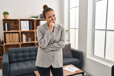 Danışma ofisinde çalışan Latin asıllı genç bir kadın kameraya kollarını kavuşturmuş ve çenesi açık bir şekilde gülümsüyor. Olumlu düşünmek. 