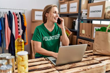Young caucasian woman wearing volunteer uniform talking on the smartphone working at charity center