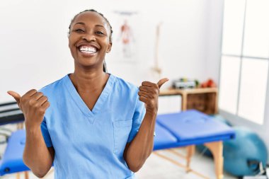 Saçları örgülü zenci bir kadın ağrı kesici kliniğinde çalışıyor. Başarılı bir jest yapıyor. Gülümsüyor ve mutlu. Neşeli ifade ve kazanan jest. 