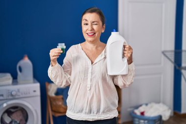 Orta yaşlı İspanyol kadın elinde deterjan şişesiyle kameraya bakıyor. Seksi bir ifadeyle, neşeli ve mutlu bir yüzle.. 
