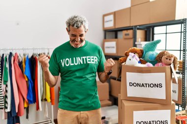 Bağışlarda gönüllü tişört giyen orta yaşlı İspanyol adam kollarını kaldırıp, gülümseyerek ve başarı için bağırarak kazanan hareketi yaparken çok mutlu ve heyecanlı duruyor. kutlama konsepti. 