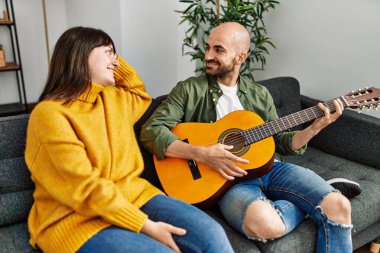 Genç İspanyol çift gülümseyerek evde kanepede oturmuş klasik gitar çalıyor..