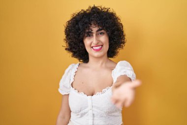 Sarı arka planda duran kıvırcık saçlı, genç esmer kadın mutlu bir şekilde gülümseyerek yardım eli uzatıyor ve kabul ediyor.. 