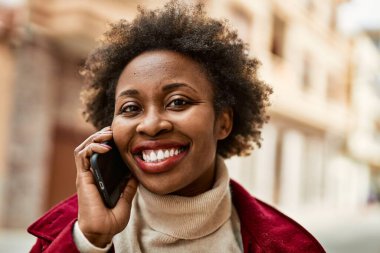 Güzel iş kadını afro saçlı Afro-Amerikan kadın mutlu ve kendinden emin bir şekilde şehirde telefonda konuşuyor.