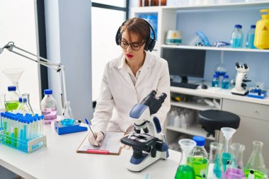 Genç beyaz kadın bilim adamı üniforması giyiyor. Laboratuvarda müzik dinliyor.