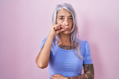 Pembe arka planda duran dövmeleri olan orta yaşlı bir kadın ağzı ve dudakları parmaklarıyla kapanan bir fermuar gibi. gizli ve sessiz, tabu konuşması 