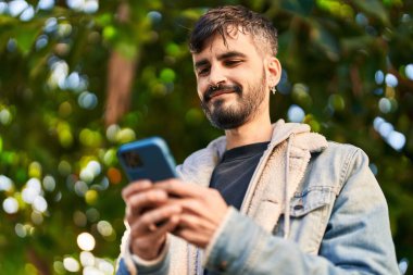 Parkta akıllı telefon kullanarak gülümseyen İspanyol genç adam.