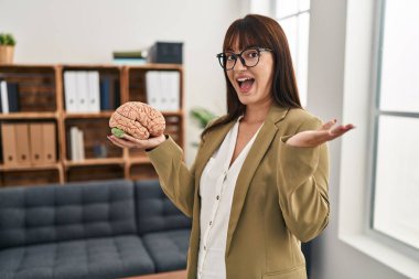 Terapi ofisinde çalışan genç terapist kadın beyni tutarak başarıyı mutlu bir gülümsemeyle ve kazanan yüz ifadesiyle kutluyor. 